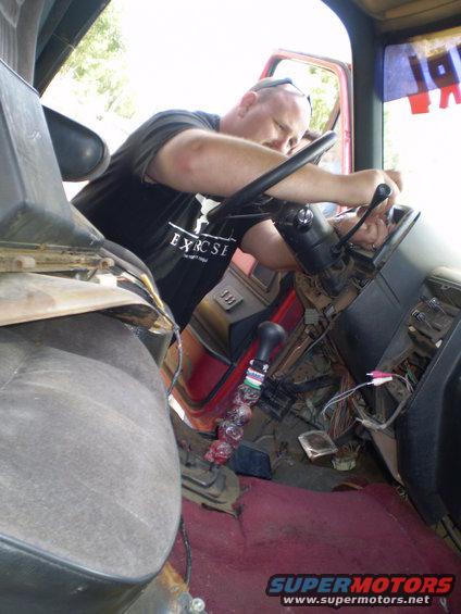 Guy working on the steering column of an old truck, wires are exposed