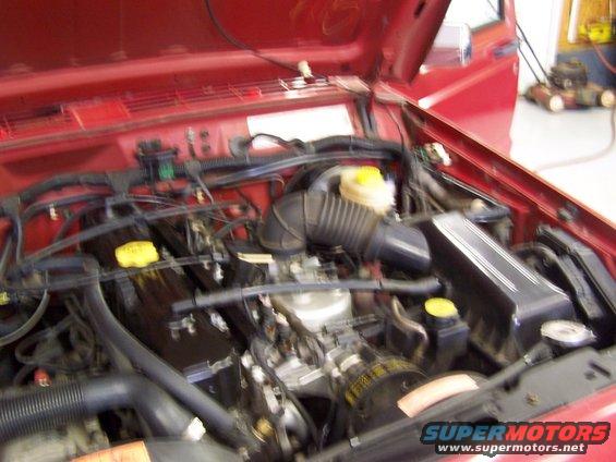 Engine bay of a red Jeep, showing the motor, hoses, and air intake. Supermotors.net logo visible