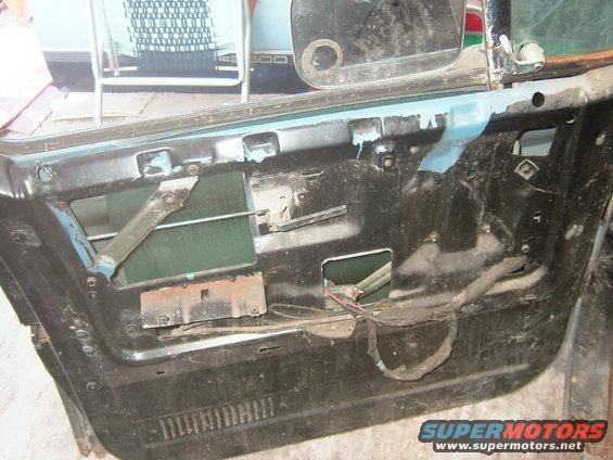 Car door interior panel removed, showing wiring and window mechanism. Blue paint visible on inner door frame