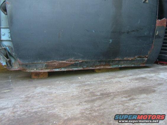 rusted rocker panel on a dark-colored truck, supported by wood blocks