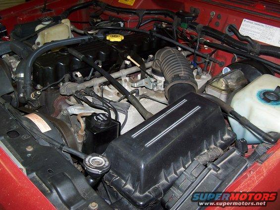 Jeep engine bay with hoses, air filter box, and power steering reservoir visible