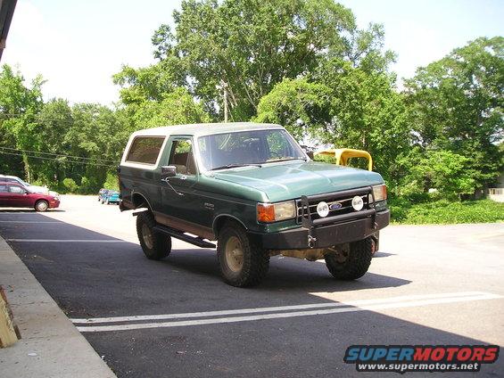 Green 1989 Ford Bronco parked on asphalt with trees in background