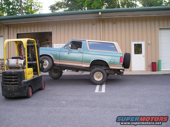 Green and tan Ford Bronco lifted on a forklift, side view