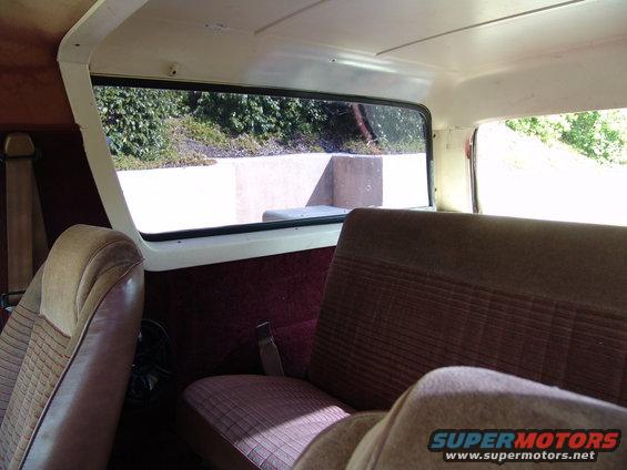 Interior shot of a vehicle showing seats and a window looking out at some bushes and concrete