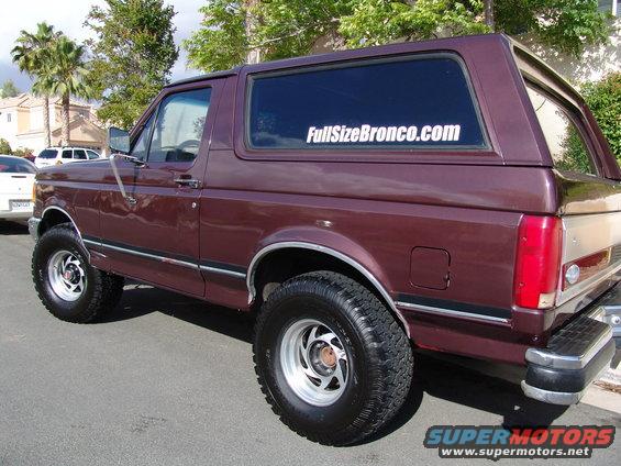 Maroon Ford Bronco with a sticker on the rear window. Visible chrome bumper and fender flares