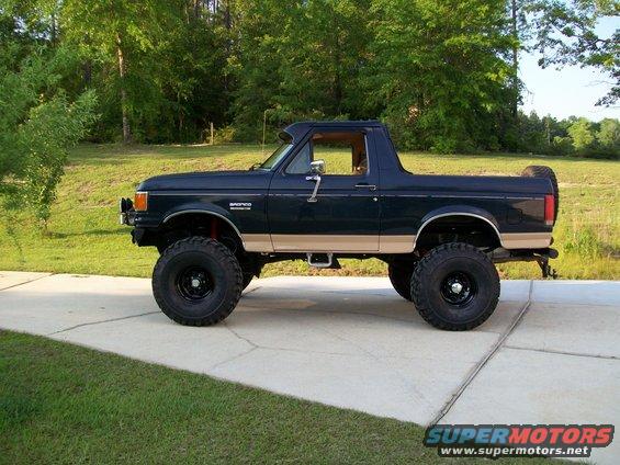 Dark blue and tan Ford Bronco with lifted suspension and large tires, seen from the side