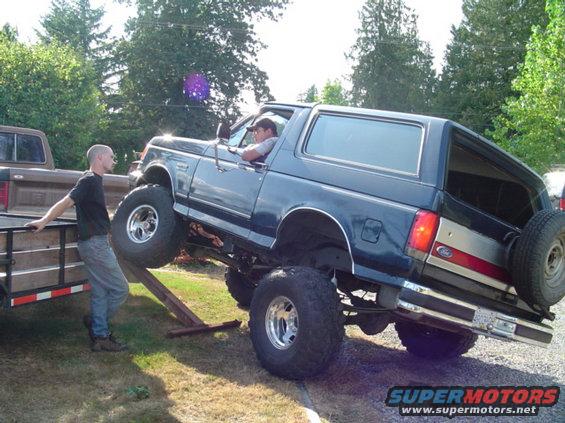 Lifted blue 1990 Ford Bronco with spare tire on rear, 3q-front view