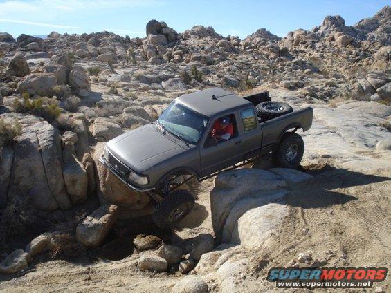 Gray pickup truck crawling over rocks on a trail. Driver is visible