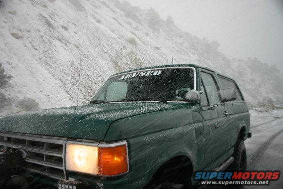 Green 1991 Ford Bronco driving in snow with 'ABUSED' sticker on windshield