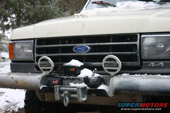 Front of a white Ford Bronco with a winch and halogen lights, covered in snow