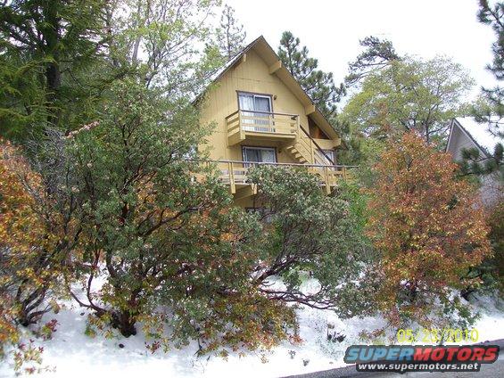Yellow house with decks and stairs on a snowy hill with trees