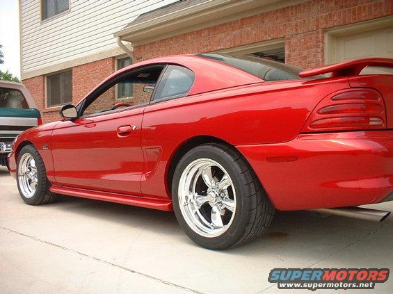 Red 1994 Ford Mustang coupe with chrome wheels and a rear spoiler, viewed from the side