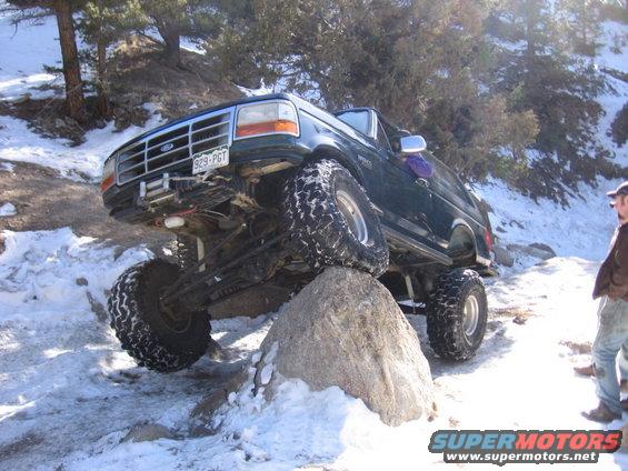 Dark green Ford Bronco with large tires on a rock, snow on the ground