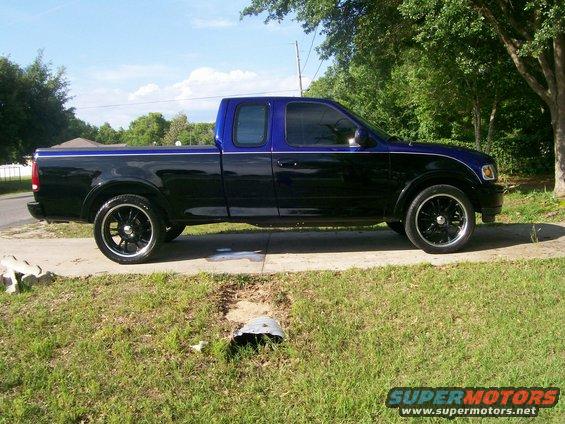 Side view of a black and blue pickup truck with custom rims parked on a driveway