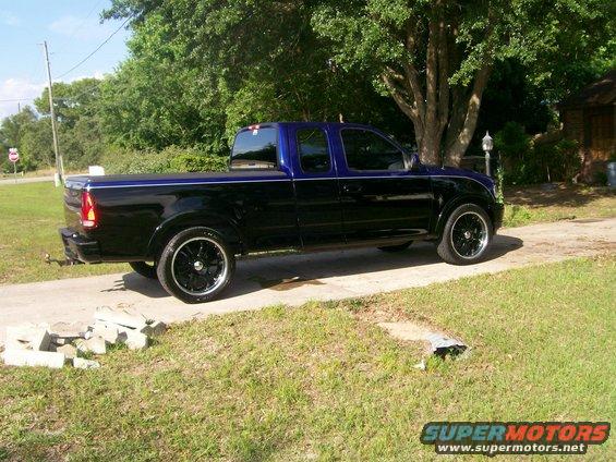 Side view of black and blue 1997 Ford F-150 pickup truck with custom wheels
