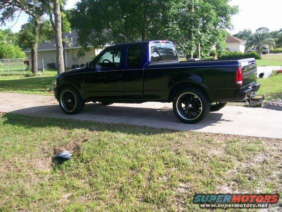 1997 Ford F-150 pickup truck, side view, dark blue with custom black wheels