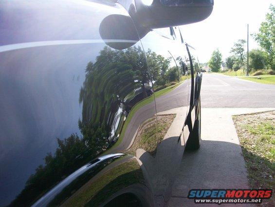 Dark pickup truck side view, reflections of trees and road on the body panel