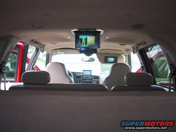 Interior view of a large SUV showing multiple screens mounted on the ceiling and dashboard