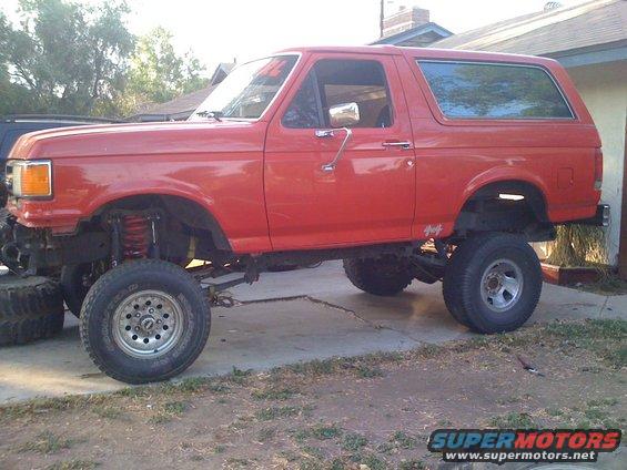 Red lifted Ford Bronco with aftermarket wheels and tires, parked on a driveway