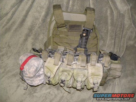Olive drab tactical vest with multiple pouches, an American flag patch, and a red-strapped pouch