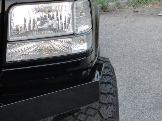 Front corner of black truck showing headlight and tire with aftermarket bumper. Likely a 1997 model