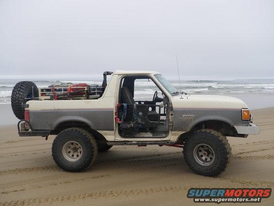 Two-tone 1991 Ford Bronco with doors removed, spare tire on back, parked on beach