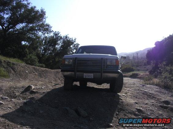 Light blue Ford Bronco on a dirt road, front view. Modified grille and bumper