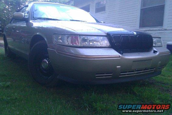 Front 3/4 view of a silver 2000 Mercury Grand Marquis parked on grass in front of a house