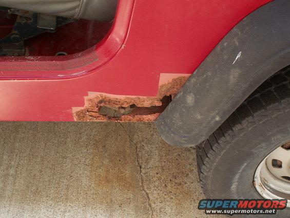 rusted out rocker panel on red vehicle next to tire