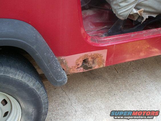 Red Jeep YJ with significant rust on the lower body panel near the rear wheel well