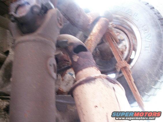 Underside view of vehicle driveshaft and exhaust system, with a tire visible