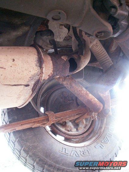 Underside view of a rusty exhaust pipe, leaf springs, and tire on a vehicle