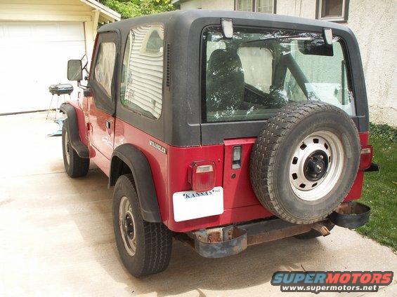 red Jeep Wrangler with black soft top, spare tire on back, Kansas plate
