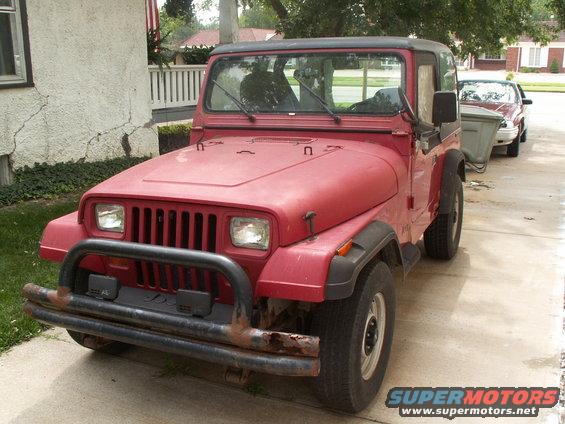 Red Jeep Wrangler with a black soft top and a rusty bull bar on the front bumper