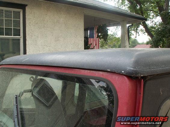 Rear of red Jeep CJ-7 with black hardtop, parked in front of house with American flag hanging on porch