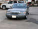 2001 Mercury Grand Marquis - A gray 2001 Mercury Grand Marquis is parked in front of a white SUV, with other vehicles in the background.