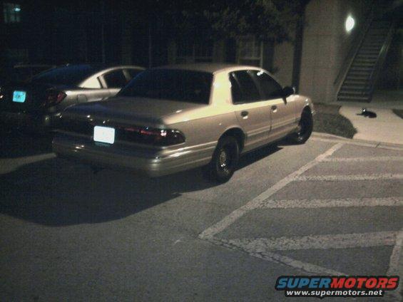 Tan sedan parked in a lot at night, rear view
