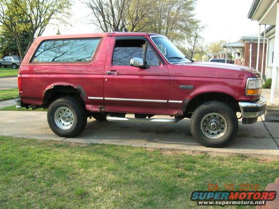 Red 1994 Ford Bronco parked on a driveway, showing rust around wheel wells