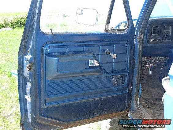 Blue interior door panel of a 1977 Ford F-250 with chrome handle and speaker grille