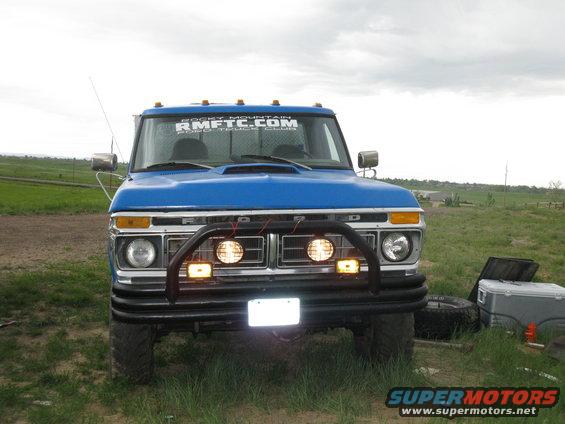 1977 Ford F-250 front view with aftermarket bull bar and auxiliary lights. "RMFTRC.COM" sticker on windshield