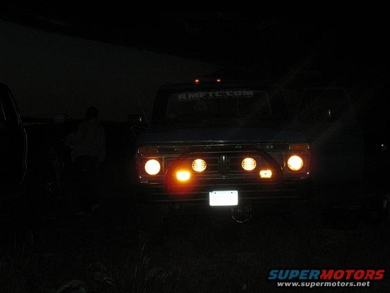 Front of a 1977 Ford F-250 with aftermarket lights on the grille. A website URL is visible on the windshield
