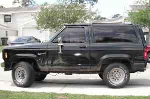 Black SUV side view, tinted windows, aftermarket wheels, some body damage