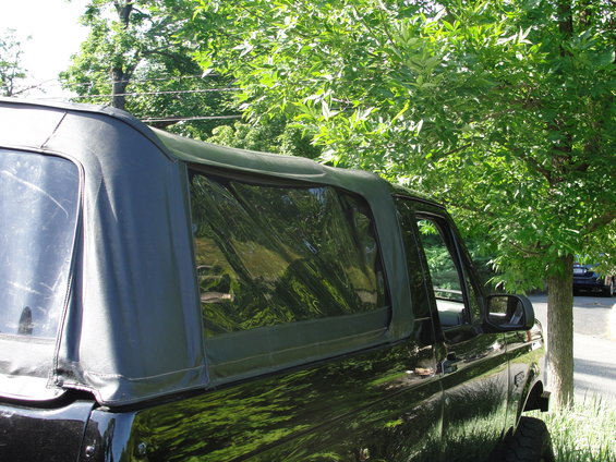 Black SUV soft top, side view. Clear plastic rear window. Trees and road in background