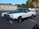 1973 Ford Ranchero - A white 1973 Ford Ranchero with a black hood and roof is parked in an asphalt lot with a building and trees in the background.