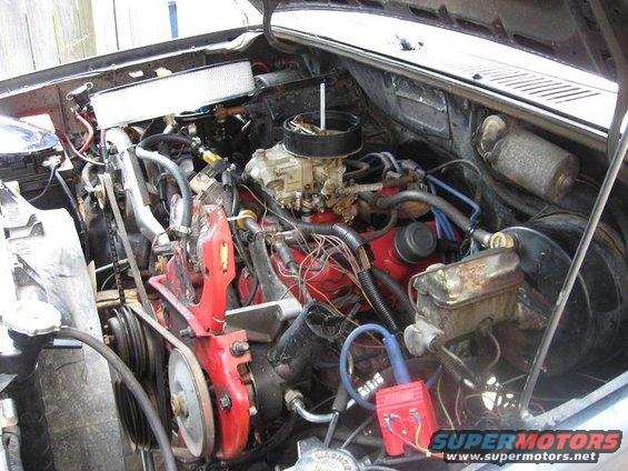 Engine bay with carburetor, air filter, and various hoses and wires visible. Some red engine components are present