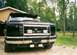 1994 Ford F-150 - Front view of a black 1994 Ford F-150, a prominent grille guard and auxiliary lights, with custom text on the visor.