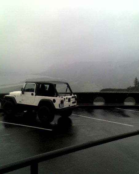 White Jeep Wrangler parked in a wet lot with a misty mountain view behind it