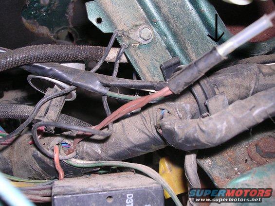 Engine wiring harness with a black zip tie and a green bracket with an arrow