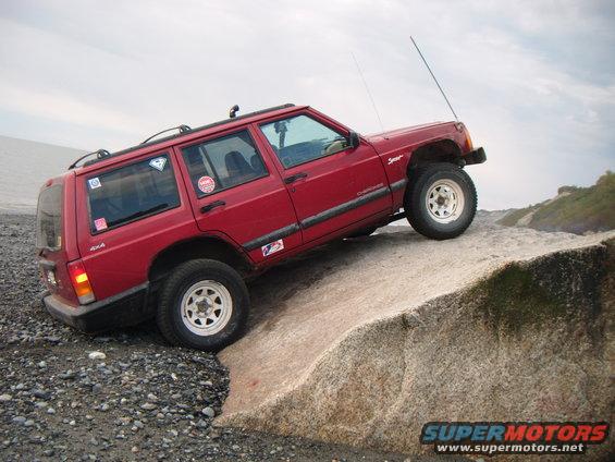Red 1998 Jeep Cherokee Sport 4x4 climbing a large rock near the water
