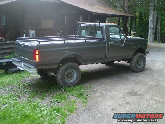 Dark gray pickup truck with a rack over the bed, parked in front of a cabin